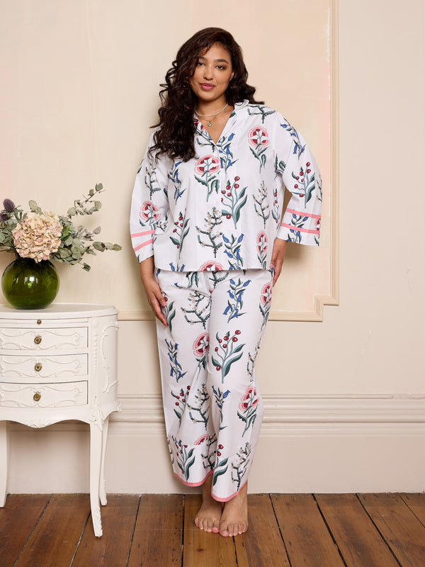 woman wearing white floral pyjama set in a cosy bedroom with a white dresser and vase with flowers