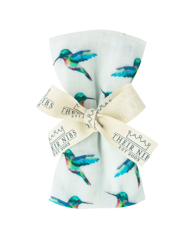 flat shot of rolled and ribbon tied cotton facecloth, white base with hand painted hummingbird pattern