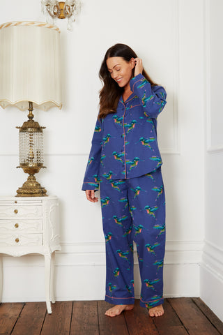 Brunette models stands wearing Navy ladies traditional pyjamas, with repeating hummingbird pattern in alternating directions, with pink piping detail. 