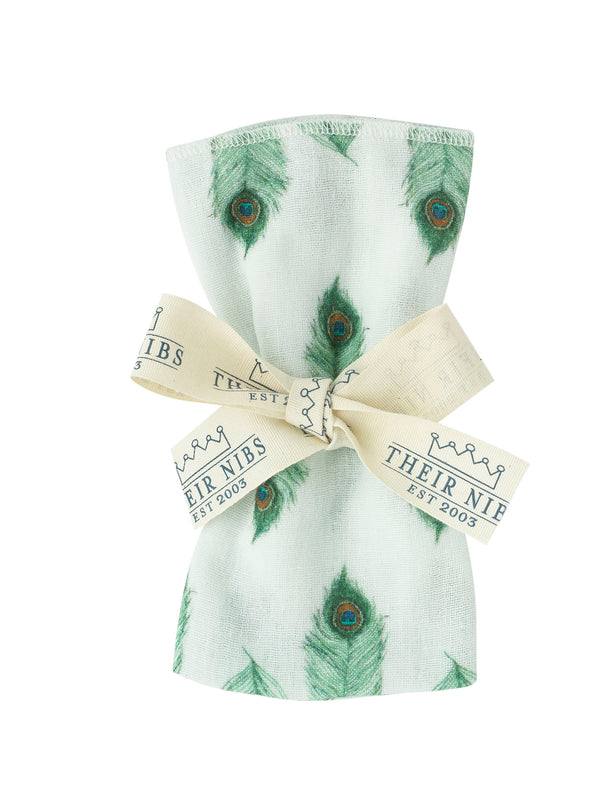 flat shot of rolled and ribbon tied cotton facecloth, white base with hand painted peacock feather pattern